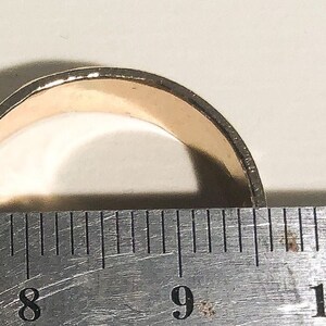 May include: A gold-colored ring is measured with a ruler. The ring is between 8 and 9 inches in diameter.
