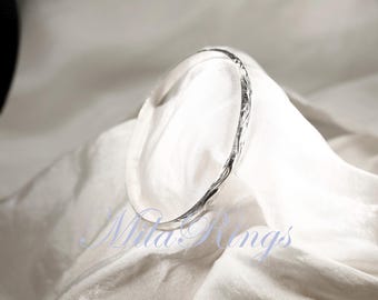 Puede incluir: Un brazalete de plata con un diseño texturizado y trenzado. El brazalete está sobre un fondo de tela blanca.