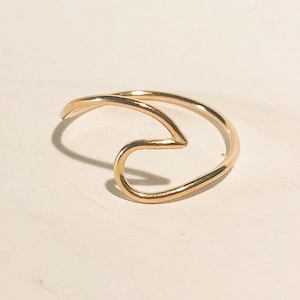 May include: A gold wave ring. The ring is made of a thin, delicate wire and is shaped like a wave.