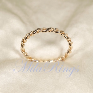 Peut inclure: Une bague dor&eacute;e avec un motif de corde torsad&eacute;e. La bague est circulaire et repose sur un tissu cr&egrave;me. Le motif de la bague est un motif continu de brins entrelac&eacute;s, cr&eacute;ant un aspect textur&eacute;. La bague est probablement en m&eacute;tal.
