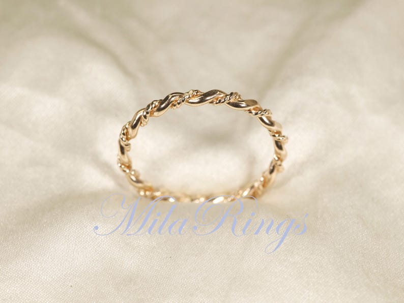 Peut inclure: Une bague dor&eacute;e avec un motif de corde torsad&eacute;e. La bague est circulaire et repose sur un tissu cr&egrave;me. Le motif de la bague est un motif continu de brins entrelac&eacute;s, cr&eacute;ant un aspect textur&eacute;. La bague est probablement en m&eacute;tal.