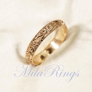 Puede incluir: Un anillo de banda de oro con un diseño floral intrincado. El anillo es delgado y delicado.