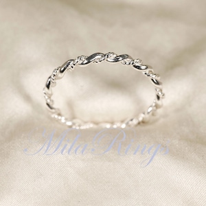 Peut inclure: Une bague argent&eacute;e avec un motif de corde torsad&eacute;e. La bague est pos&eacute;e sur un fond blanc cass&eacute; doux. Le design de la bague pr&eacute;sente des brins entrelac&eacute;s, cr&eacute;ant un aspect textur&eacute; et &eacute;l&eacute;gant. C'est un bijou d&eacute;licat.