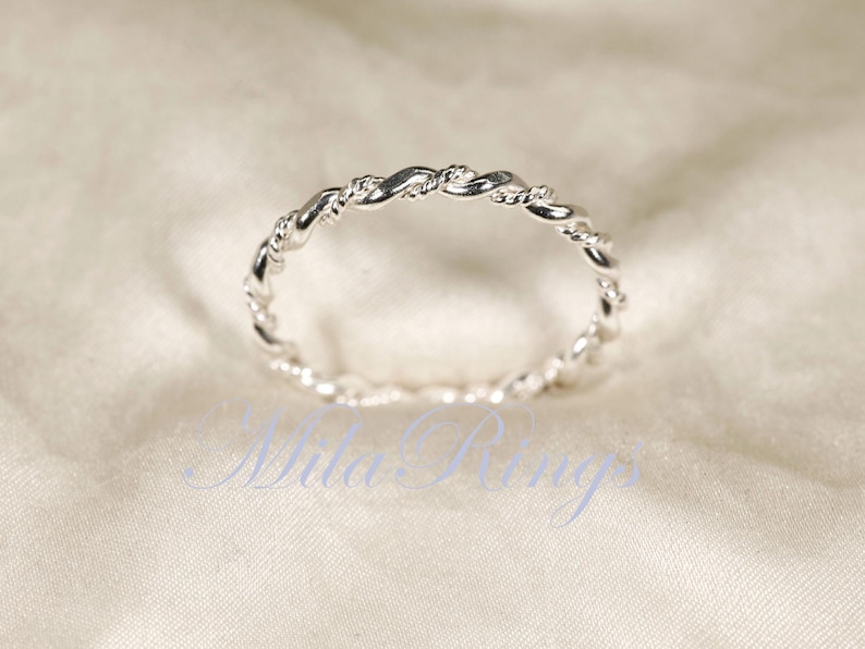 Peut inclure: Une bague argent&eacute;e avec un motif de corde torsad&eacute;e. La bague est pos&eacute;e sur un fond blanc cass&eacute; doux. Le design de la bague pr&eacute;sente des brins entrelac&eacute;s, cr&eacute;ant un aspect textur&eacute; et &eacute;l&eacute;gant. C'est un bijou d&eacute;licat.