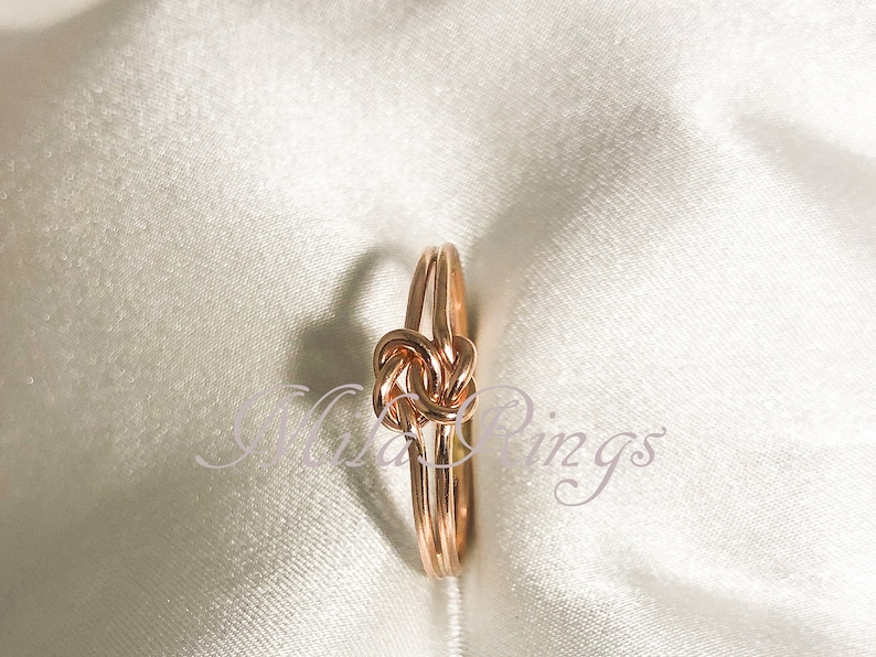 Op de afbeelding: Een knoop ring van ros&eacute;goud met een eenvoudig ontwerp. De ring is gemaakt van twee dunne banden van metaal die samen gedraaid zijn om een knoop te vormen.