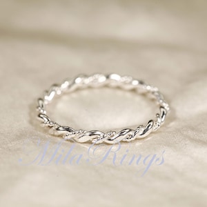 Peut inclure: Une bague argent&eacute;e avec un motif de corde torsad&eacute;e. La bague est circulaire et repose sur une surface de couleur claire. Le motif de la bague est un motif continu de brins entrelac&eacute;s.