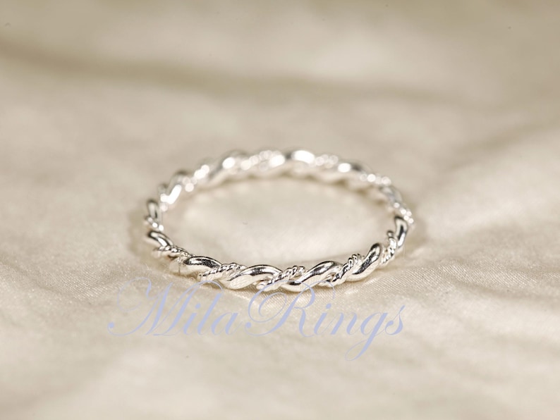 Peut inclure: Une bague argent&eacute;e avec un motif de corde torsad&eacute;e. La bague est circulaire et repose sur une surface de couleur claire. Le motif de la bague est un motif continu de brins entrelac&eacute;s.