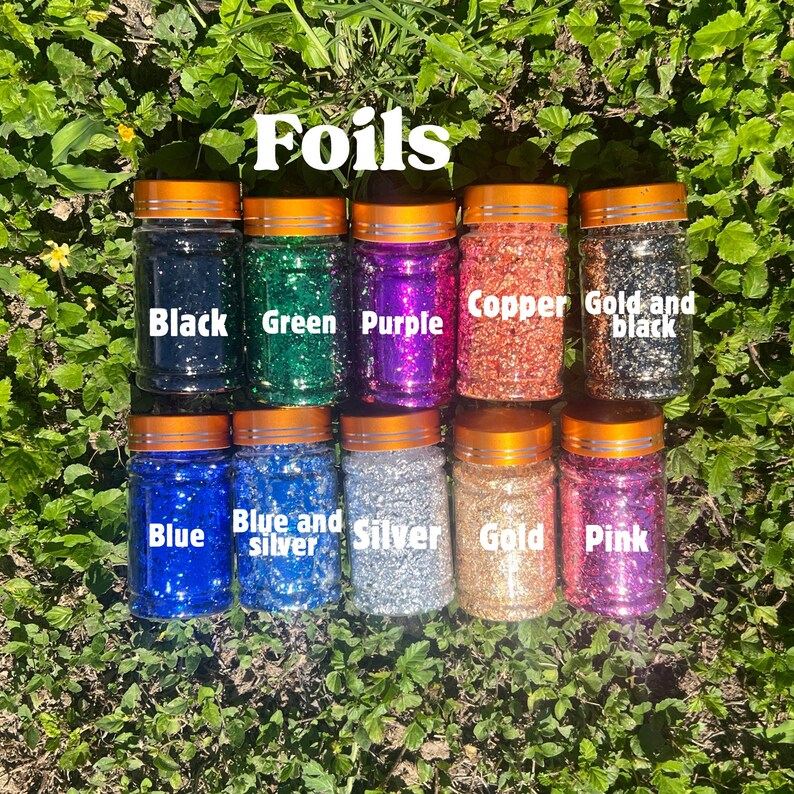 May include: Ten clear plastic jars with orange lids containing decorative foils in various colors. The jars are labeled with the text Foils and individual color names: Black, Green, Purple, Copper, Gold and black, Blue, Blue and silver, Silver, Gold, and Pink.