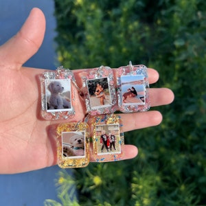May include: Five rectangular resin keychains featuring embedded photographs and metallic flakes. Three keychains contain silver flakes with pink accents, while two feature gold flakes. Each keychain displays a unique personal photo.