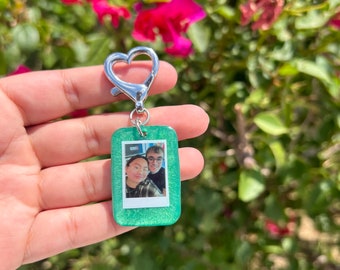 May include: A green glitter keychain with a photo of a couple inside a clear plastic frame. The keychain has a silver heart-shaped clasp.