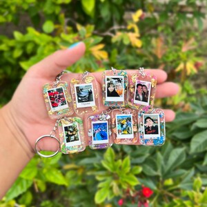 May include: A collection of seven rectangular resin keychains, each featuring a miniature photograph framed within clear resin embedded with colorful glitter and small butterfly-shaped accents. Each keychain includes a silver metal split ring.