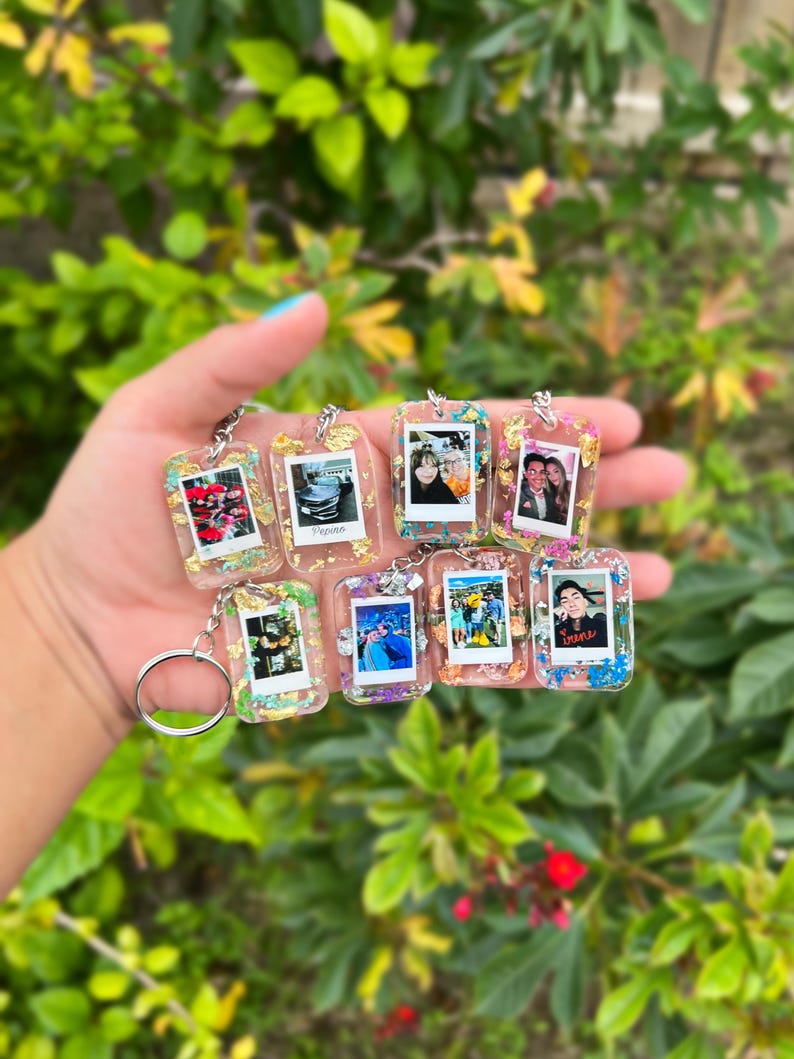 May include: A collection of seven rectangular resin keychains, each featuring a miniature photograph framed within clear resin embedded with colorful glitter and small butterfly-shaped accents. Each keychain includes a silver metal split ring.