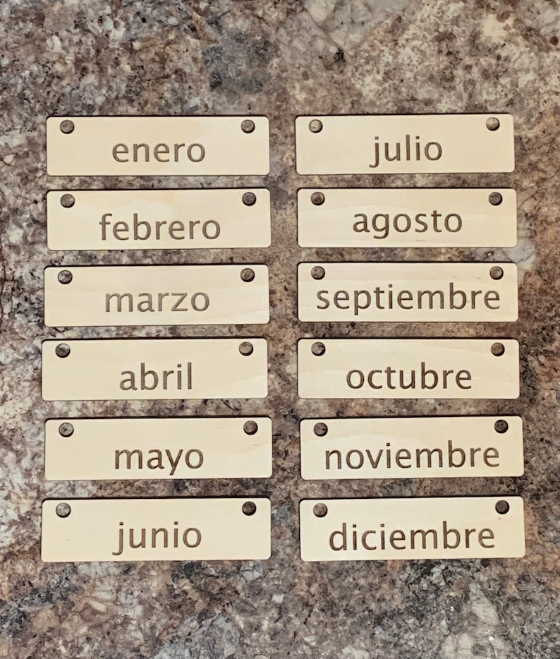 May include: Twelve wooden tags with the names of the months of the year in Spanish. The tags are light brown and have two holes at the top.