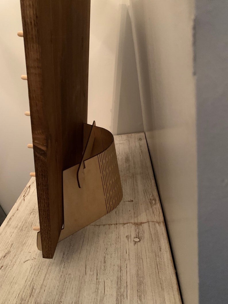 Pode incluir: Uma placa de madeira com um suporte. A placa &eacute; marrom e tem um acabamento de madeira natural. O suporte &eacute; feito de madeira clara e tem uma forma curva.