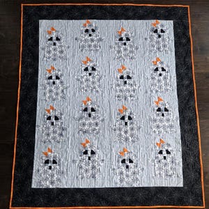 May include: A handmade quilt featuring a repeating pattern of ghost figures with orange bows. The ghosts are white with black eyes and mouths, set against a light blue background. The quilt has a black border with an orange trim and spiderweb design.