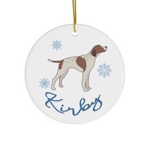 May include: A white ceramic Christmas ornament with a brown and white dog illustration, blue snowflakes, and the name "Kirby" written in blue cursive.