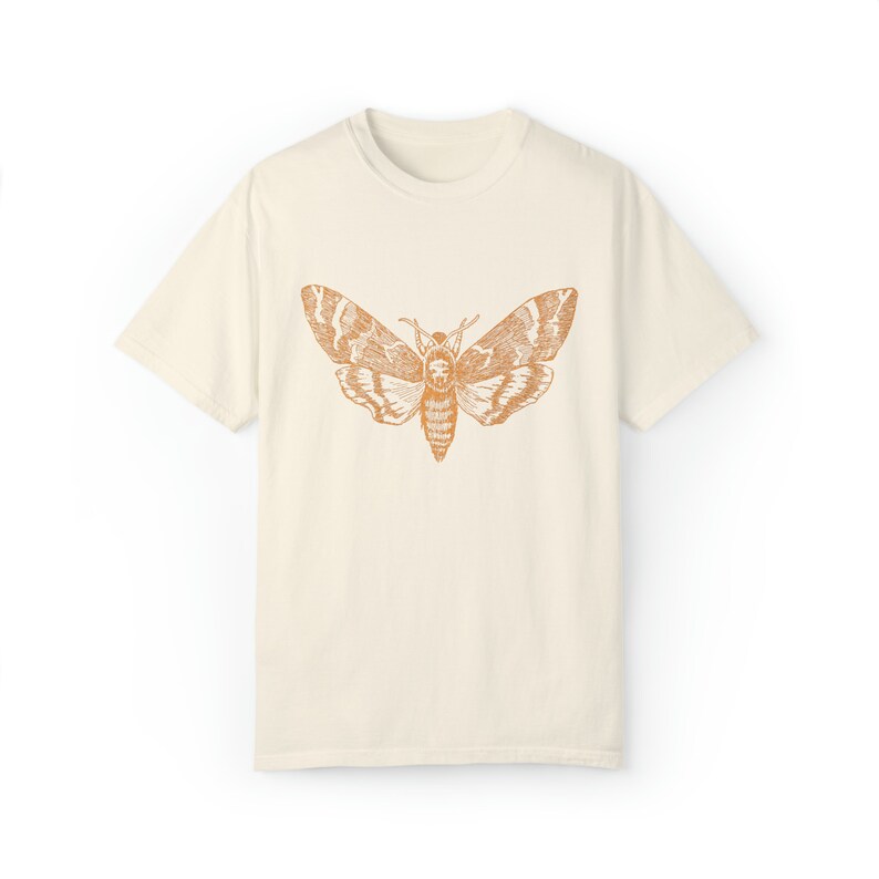 May include: A cream colored t-shirt with a vintage illustration of a moth in orange on the front.