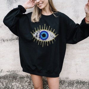 May include: Black sweatshirt with a large blue and white eye graphic. The eye has a gold outline and is surrounded by gold rays.