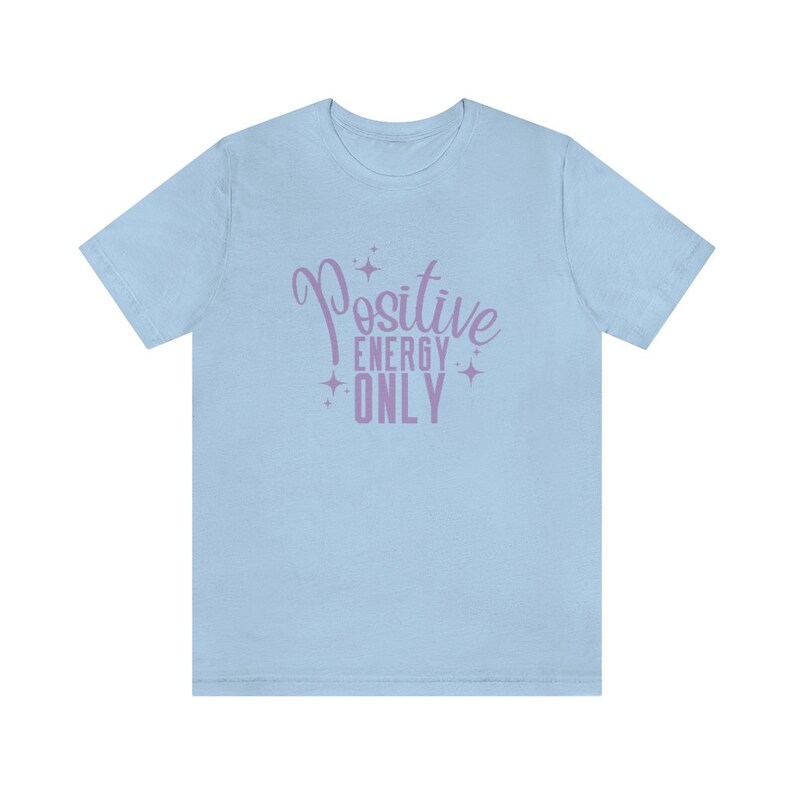 Op de afbeelding: Lichtblauw T-shirt met een paarse grafische afbeelding met de tekst "Positive Energy Only" met sterren rond de tekst.