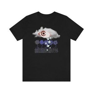 May include: Black t-shirt with a graphic of a large eye in a cloud raining small white cats onto a field of blue flowers.