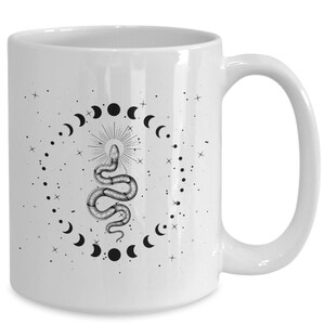 Pode incluir: Caneca de cer&acirc;mica branca com uma ilustra&ccedil;&atilde;o em preto e branco de uma cobra com um design de lua e estrelas.