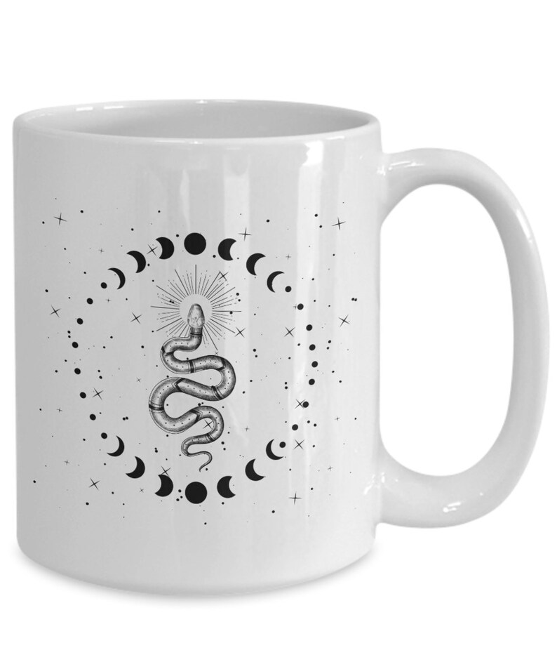 Pode incluir: Caneca de cer&acirc;mica branca com uma ilustra&ccedil;&atilde;o em preto e branco de uma cobra com um design de lua e estrelas.
