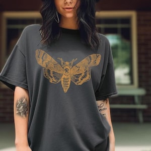 May include: A dark gray t-shirt with a vintage illustration of a moth in a yellow-gold color. The moth is centered on the shirt.