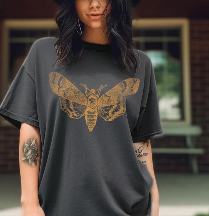 May include: A dark gray t-shirt with a vintage illustration of a moth in a yellow-gold color. The moth is centered on the shirt.