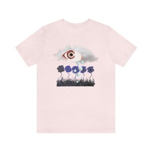 May include: Pink t-shirt with a graphic of a large eye in a cloud crying small white eyes onto a field of blue flowers.