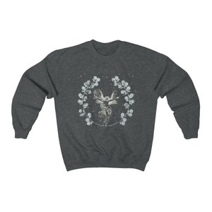 May include: A dark heather grey sweatshirt with a white graphic of a fairy flying inside a wreath of flowers.
