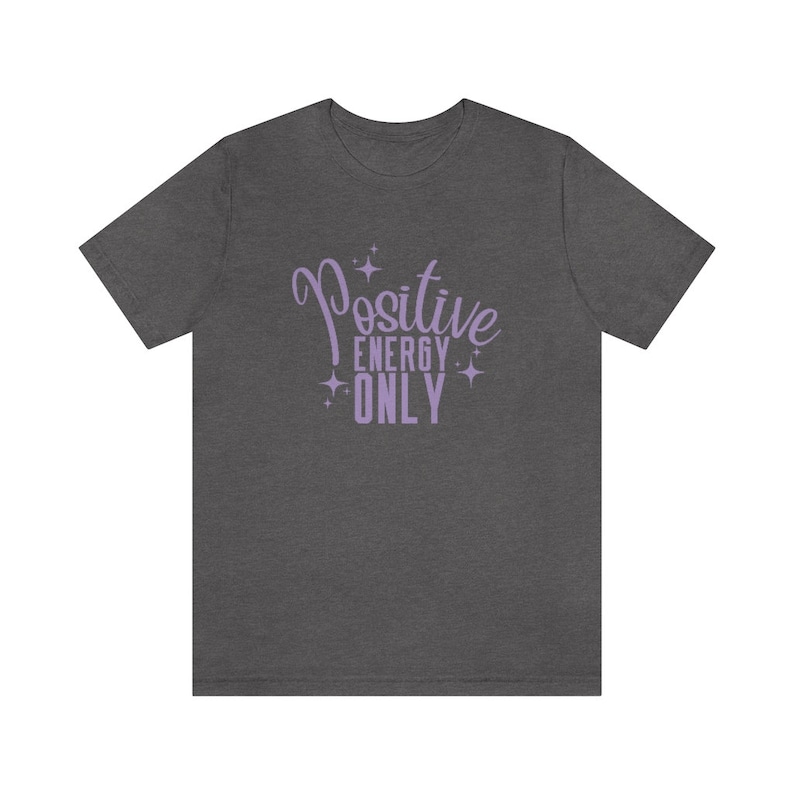 Op de afbeelding: Een donker grijs t-shirt met de tekst "Positive Energy Only" in paarse letters met glinsterende sterren.