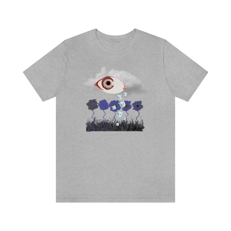 May include: A gray t-shirt with a graphic of a large eye crying small white cats onto a field of blue flowers.