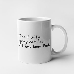 May include: White ceramic mug with black text that reads "The fluffy gray cat lies. It has been fed."