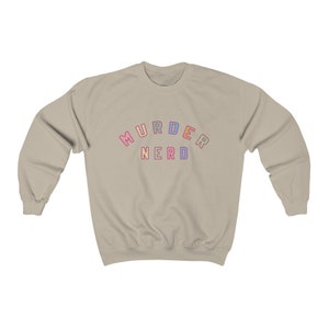 May include: A light beige sweatshirt with the text "MURDER NERDO" in rainbow colors.