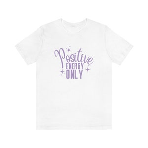 Op de afbeelding: Wit T-shirt met een paars ontwerp met de tekst "Positive Energy Only" met sterren rond de tekst.