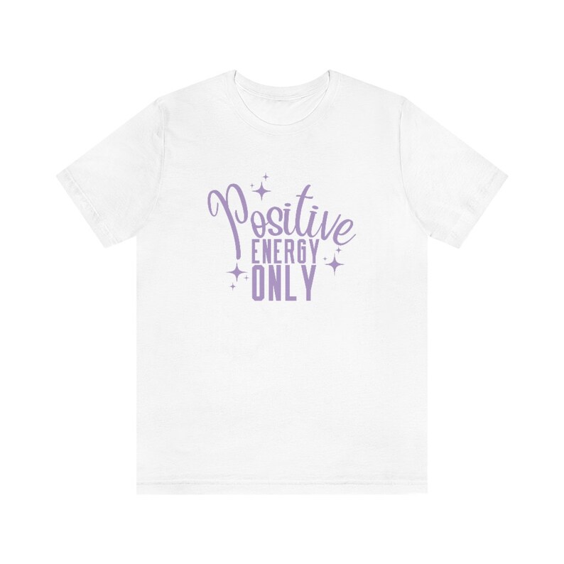 Op de afbeelding: Wit T-shirt met een paars ontwerp met de tekst "Positive Energy Only" met sterren rond de tekst.