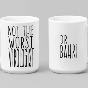 May include: Two white ceramic mugs with black text. One mug says "Not the worst virologist" and the other mug says "Dr Bahri".