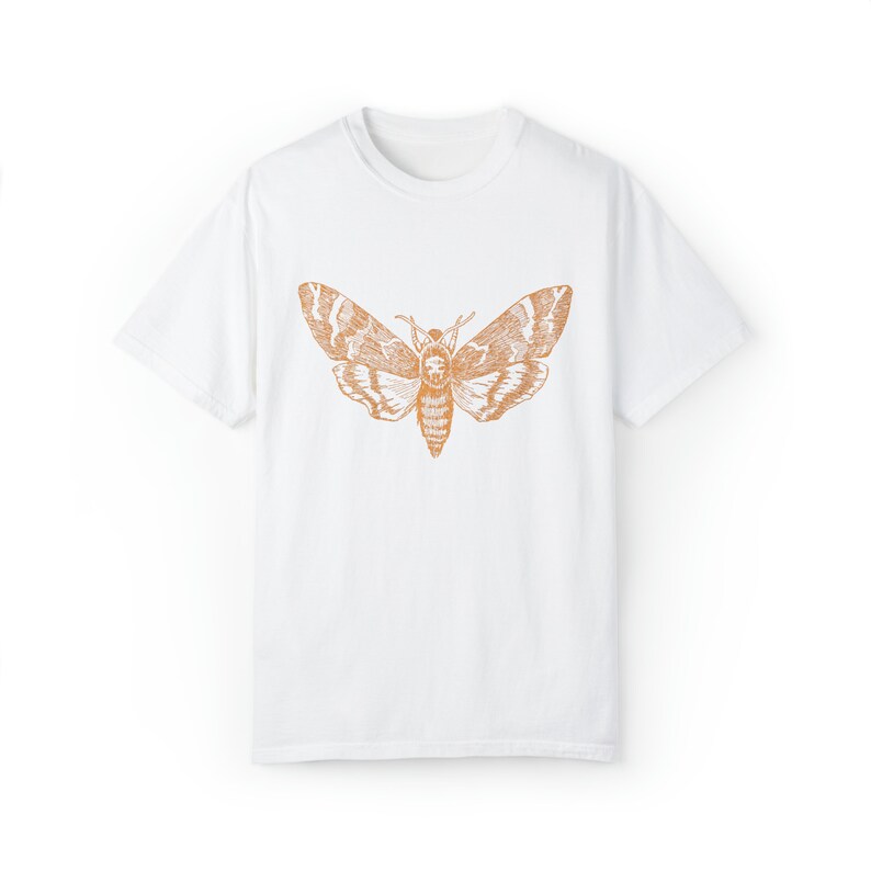 May include: White t-shirt with a brown outline of a moth printed on the front.