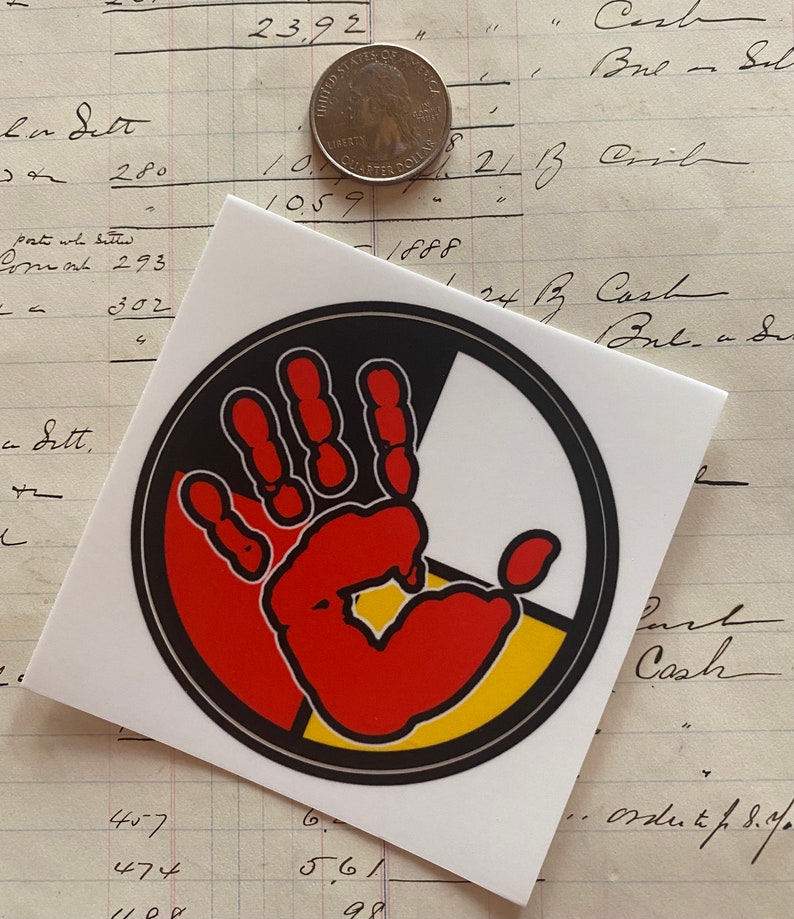 May include: A round sticker with a black outline and a red handprint in the center. The handprint is surrounded by four colored sections: black, red, yellow, and white. The sticker is on a white background.