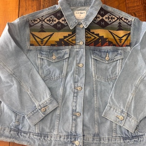 May include: A light blue denim jacket with a colorful geometric pattern on the shoulders. The jacket has a button closure and two front pockets. The label on the jacket reads "Old Navy" and "M".