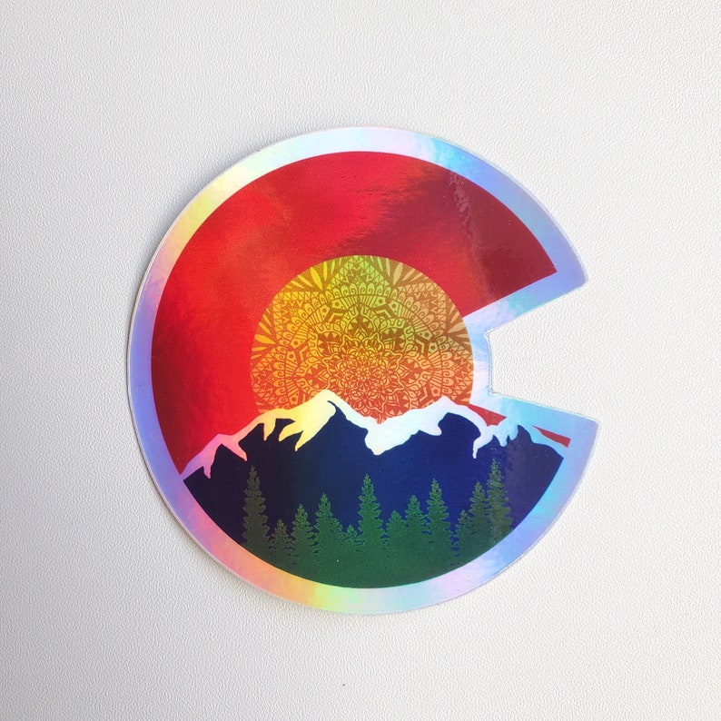 May include: A holographic sticker featuring a red, yellow, and blue outline of the state of Colorado. The outline is filled with a mandala design and a mountain range with pine trees.