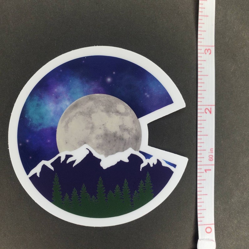 May include: A sticker featuring a stylized outline of the state of Colorado with a full moon, mountains, and a starry night sky.