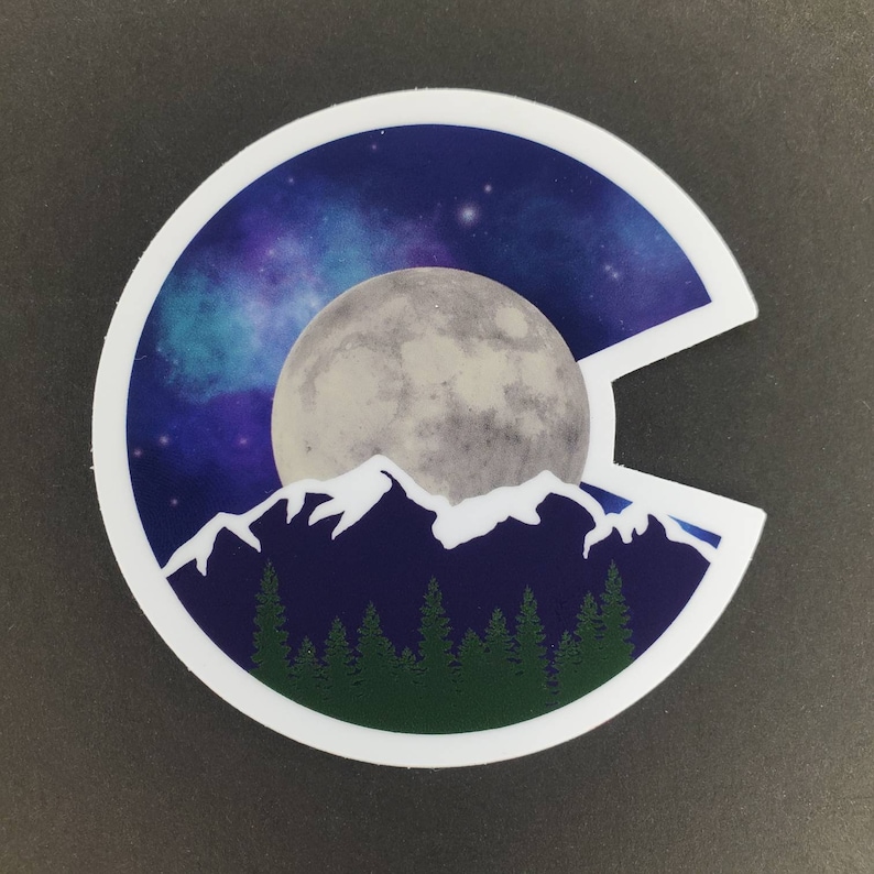 May include: A white sticker with a blue, purple, and white starry sky background. A large, gray moon is in the center of the sticker. A white mountain range is in front of the moon, and a dark blue mountain range is behind the moon. A row of dark green trees is at the bottom of the sticker.