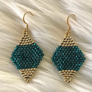 Puede incluir: Un par de pendientes de cuentas verdes y doradas con forma de diamante. Los pendientes están hechos con cuentas pequeñas y redondas y tienen un gancho dorado.