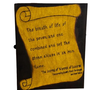 Puede incluir: Una caja de madera con un diseño en forma de rollo en la parte delantera. El rollo es amarillo y tiene texto negro que dice: "The breath of life of the seven and one combined and set the stone ablaze in an iron flame. The Journal of Warrick of Luceras Translated by Cadets Violet Sornangail and Dain Aetos".