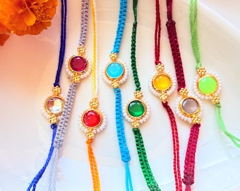 May include: A collection of seven colourful braided cord bracelets, each featuring a central round gemstone in shades of red, blue, green, yellow, and clear, surrounded by small white beads and gold-toned metal accents on thin adjustable strings.