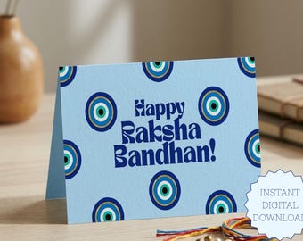 May include: A light blue greeting card featuring a repeating pattern of dark blue, white, and turquoise evil eye symbols. The text "Happy Raksha Bandhan!" is printed in a bold, dark blue font in the centre of the card.