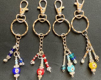 May include: Four silver keyrings with beaded charms. Each keyring has a silver ring and a silver clasp. The charms are made of colourful beads and a round, sparkly, multi-coloured bead.