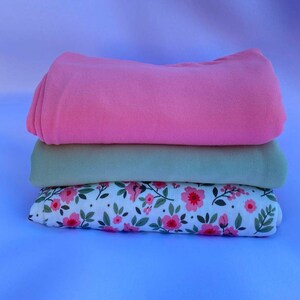 May include: Three fabric swatches stacked on top of each other. The top swatch is pink, the middle swatch is light green, and the bottom swatch is white with a pink floral pattern.