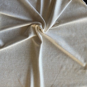 May include: A close-up of a beige textured fabric with a woven pattern. The fabric is folded and draped, creating a soft and inviting look.